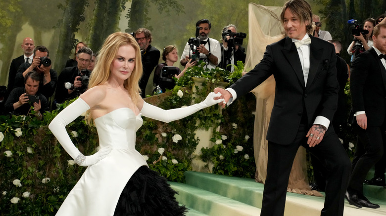 Nicole Kidman posing in a white strapless gown with white opera gloves taking Keith Urban's hand at an event in 2024.