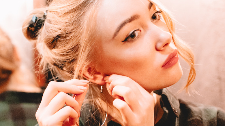 blond female puts on danglers earrings 