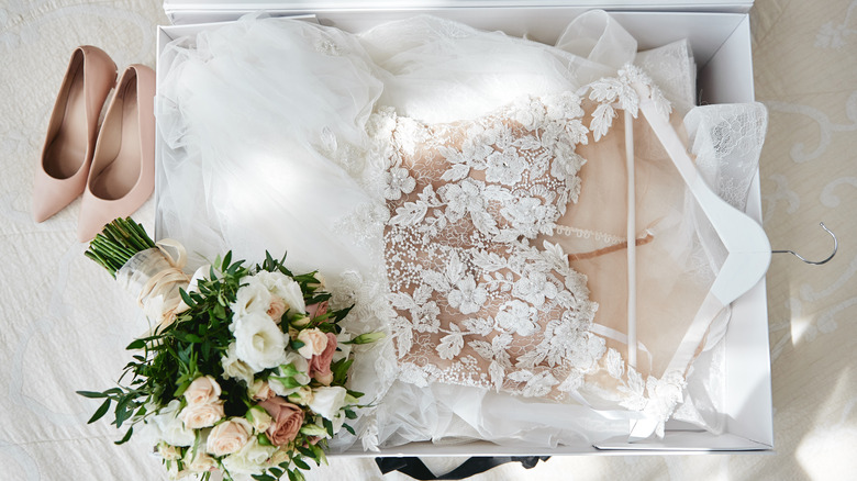 wedding dress in a box with a bouquet and pair of heels