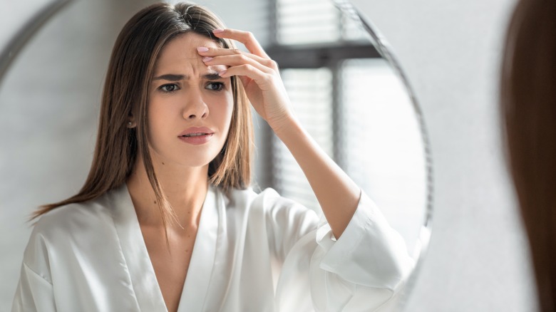 Woman inspects forehead in mirror 