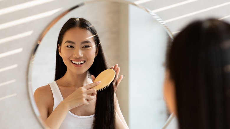 woman happily standing in front of mirror, brushing hair