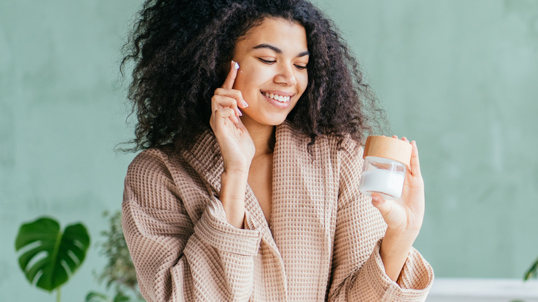 woman in bathrobe applying face cream 