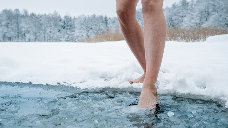 person dipping their foot into ice water hole in the winter