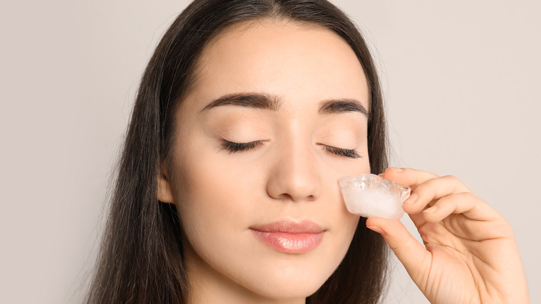 Woman rubbing ice cube on face 