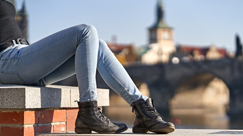 Woman in skinny jeans and boots sitting on wall
