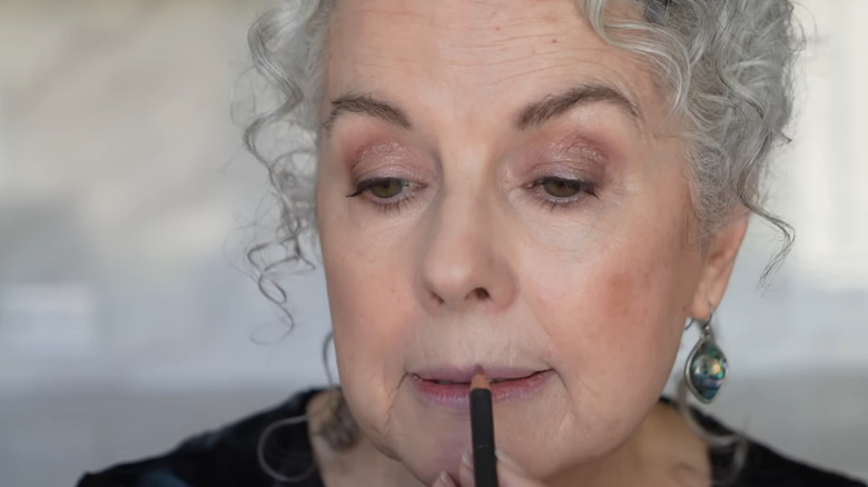 Older woman with curly gray hair applying lip liner