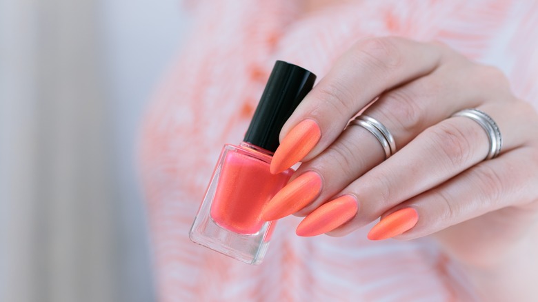 Person with orange nails holding polish bottle