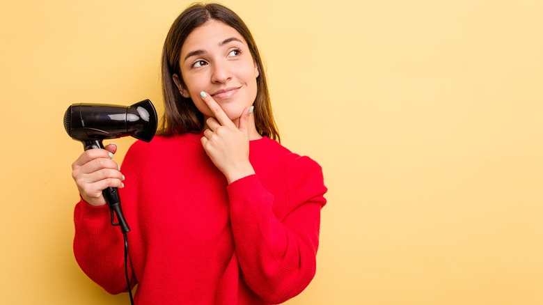 Woman contemplating holding hairdryer