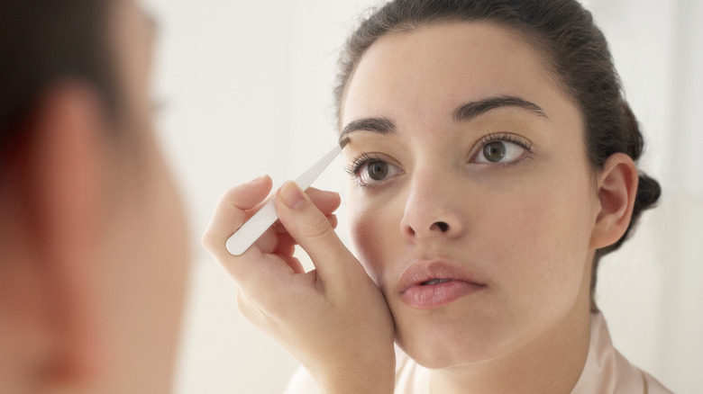 Woman plucking eyebrows in mirror