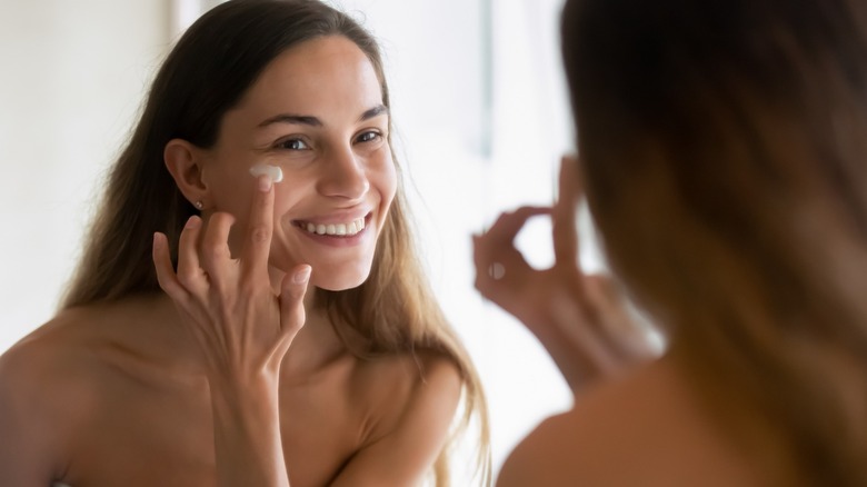 Smiling woman applying facial moisturizer