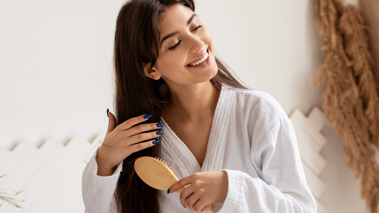 woman sitting on edge of bathtub brushing hair