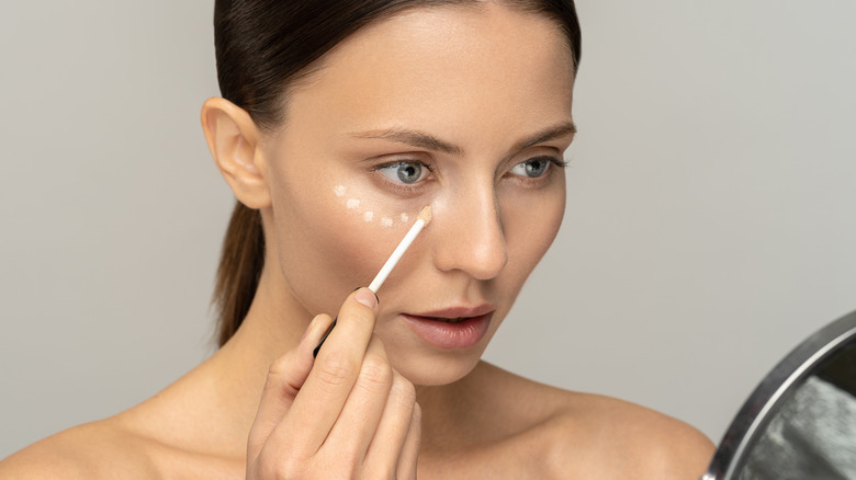 woman looking in mirror applying concealer