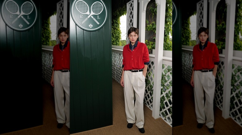 Emma Corrin wears a slouchy polo shirt and tie with white suit pants to Wimbledon 2026