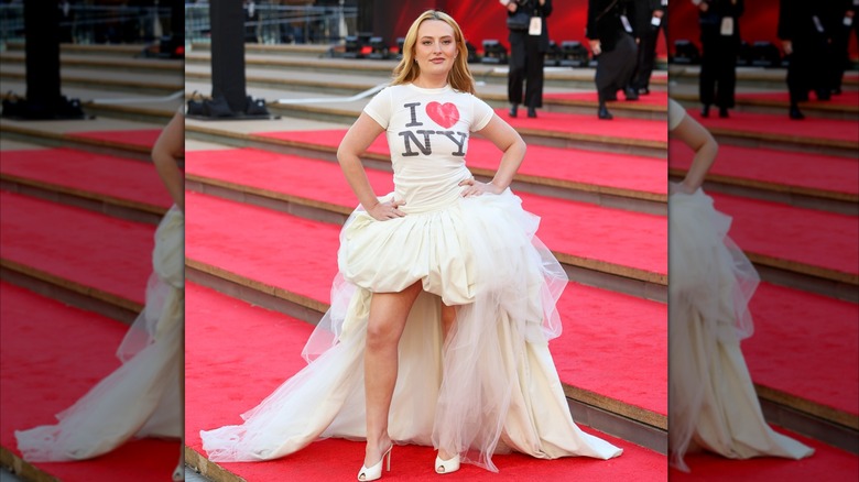 Amelia ﻿Dimoldenberg at the DWP2 premiere. She is a young woman with fair skin and blonde hair. She is wearing a white t-shirt with "I Heart NY" printed on it, a white bubble skirt with a tulle train, and white heels.