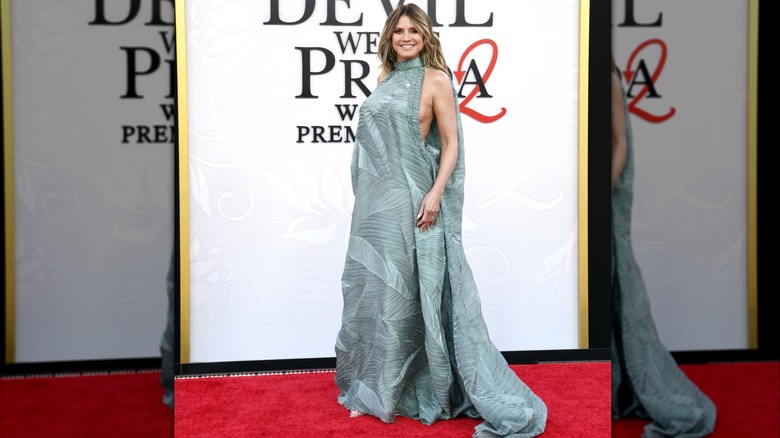 Heidi Klum at the DWP2 premiere. She is a woman with fair skin and blonde hair. She is wearing a seafoam green sleeveless high-neck gown with revealing side cut-outs, accordion-pleated designs, and a wide, flowing train.