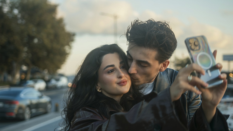 A woman taking a selfie as a man kisses her