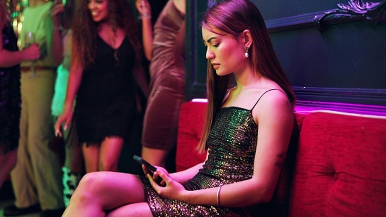 A woman checking her phone in a club after being ghosted