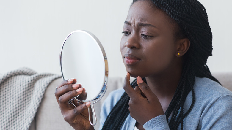Woman concerned about jawline acne in mirror