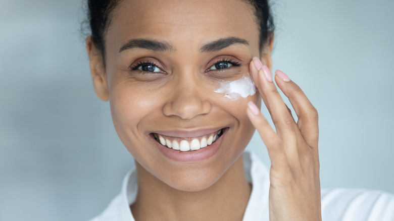 smiling woman applying cream on cheek