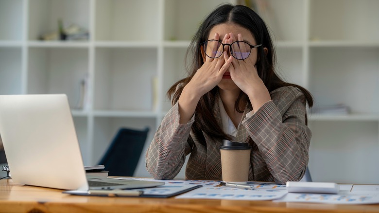 stressed woman at desk with hands over eyes