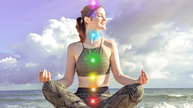 Woman meditating on beach with glowing chakras