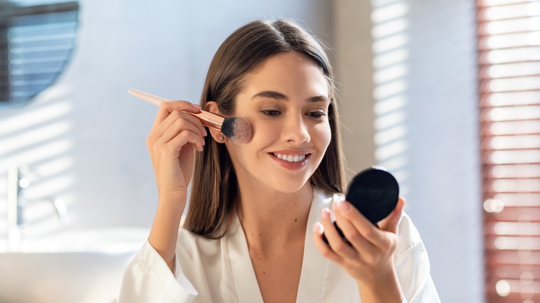 young woman applying blush with a brush 