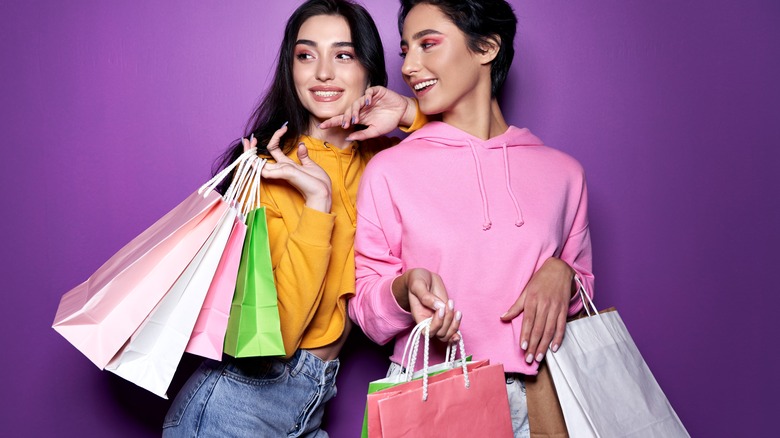 Two friends carrying shopping bags against purple backdrop