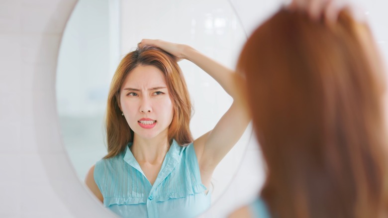 Woman with oily hair looking in the mirror