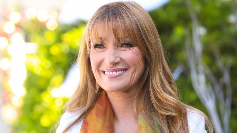 Jane Seymour smiling outside with wavy hair wearing a white top with a colorful scarf.