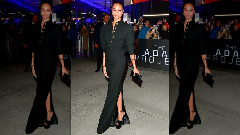 Zoe Saldaña posing at a premiere wearing a long black dress with buttons.