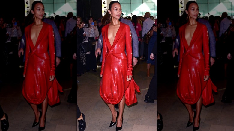 Zoe Saldaña looking to the side at an event wearing a sparkly red dress with a deep-v neckline.