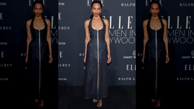 Zoe Saldaña posing at an event wearing a denim halter-top dress with a zipper up the middle.