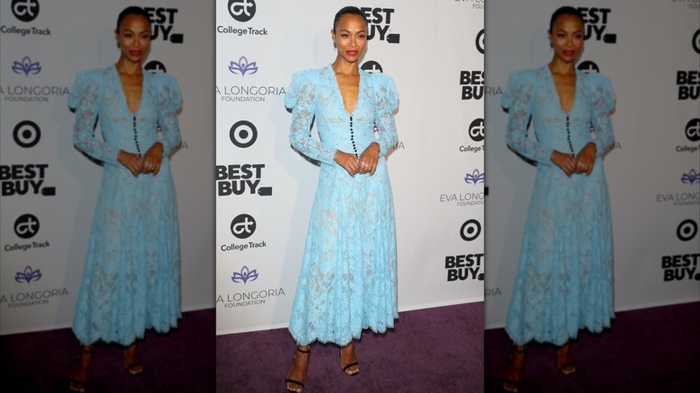 Zoe Saldaña posing at an event wearing a light-blue lace dress with poofy shoulders.