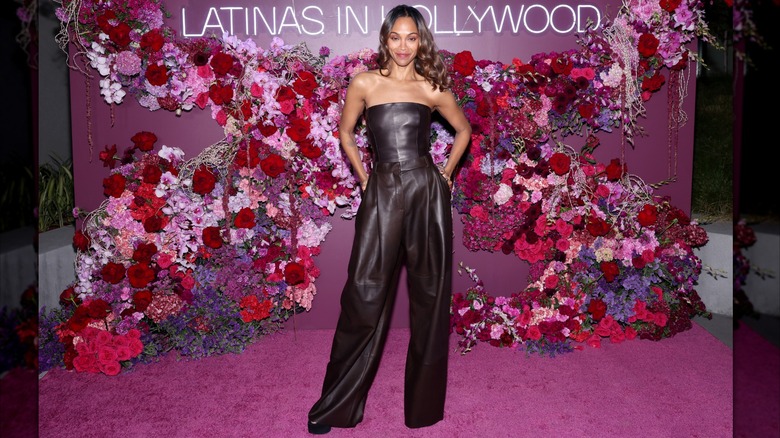 Zoe Saldaña posing at an event wearing a strapless brown leather jumpsuit.