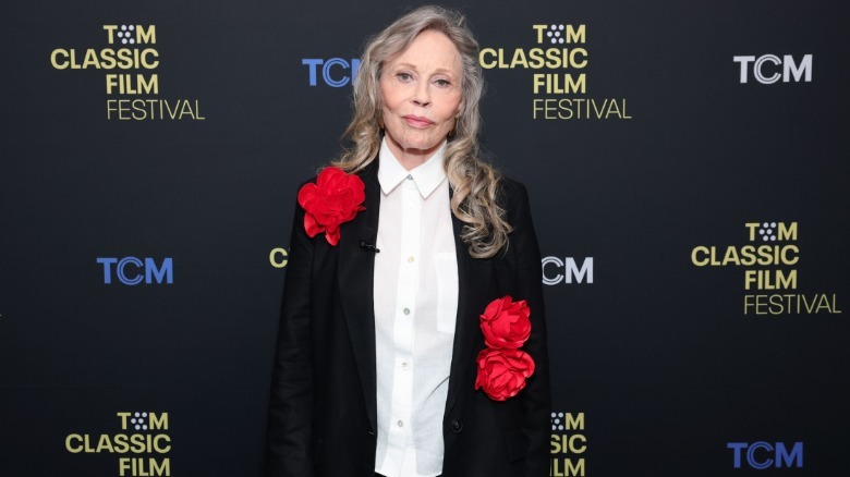 Faye Dunaway wearing a white collared shirt with a black jacket featuring large rose appliqués