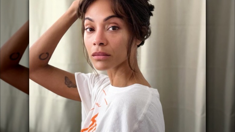 Makeup-free Zoe Saldana in a white t-shirt holding her hair up