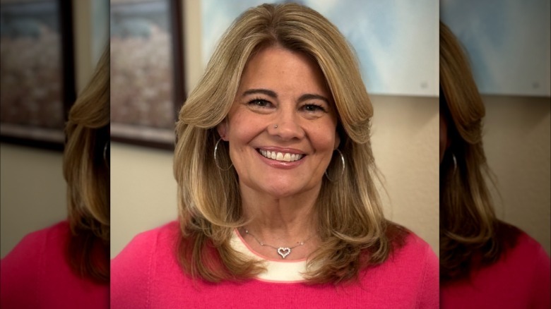 Lisa Whelchel smiles for a photo wearing a pink sweater and silver jewelry