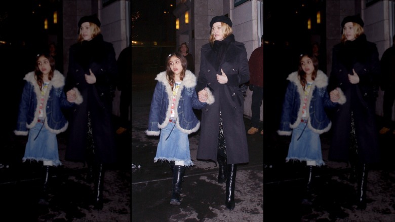 Lourdes Leon wears a denim ensemble while holding hands with Madonna who wears a gray trench coat and leather boots.